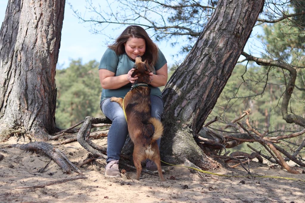 Hundetrainerin Magda Popiela sitzt mit einem Hund unter Bäumen